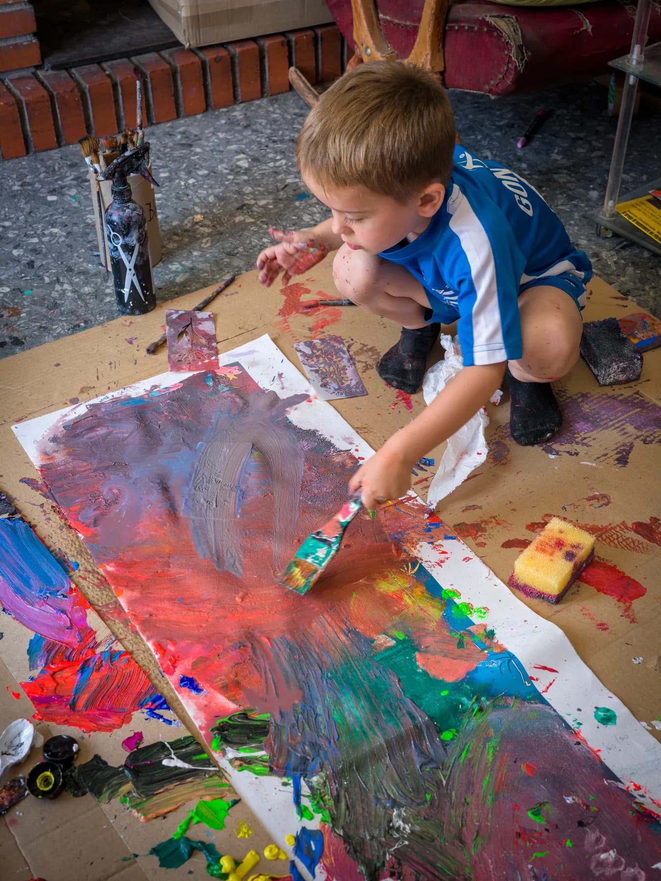 Gonzalo paints on the studio floor, surrounded by colours.